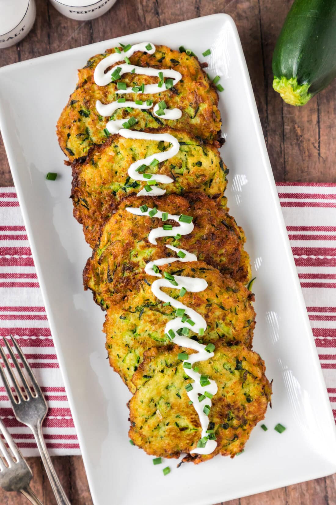 Zucchini Fritters on a platter with sour cream drizzled on top