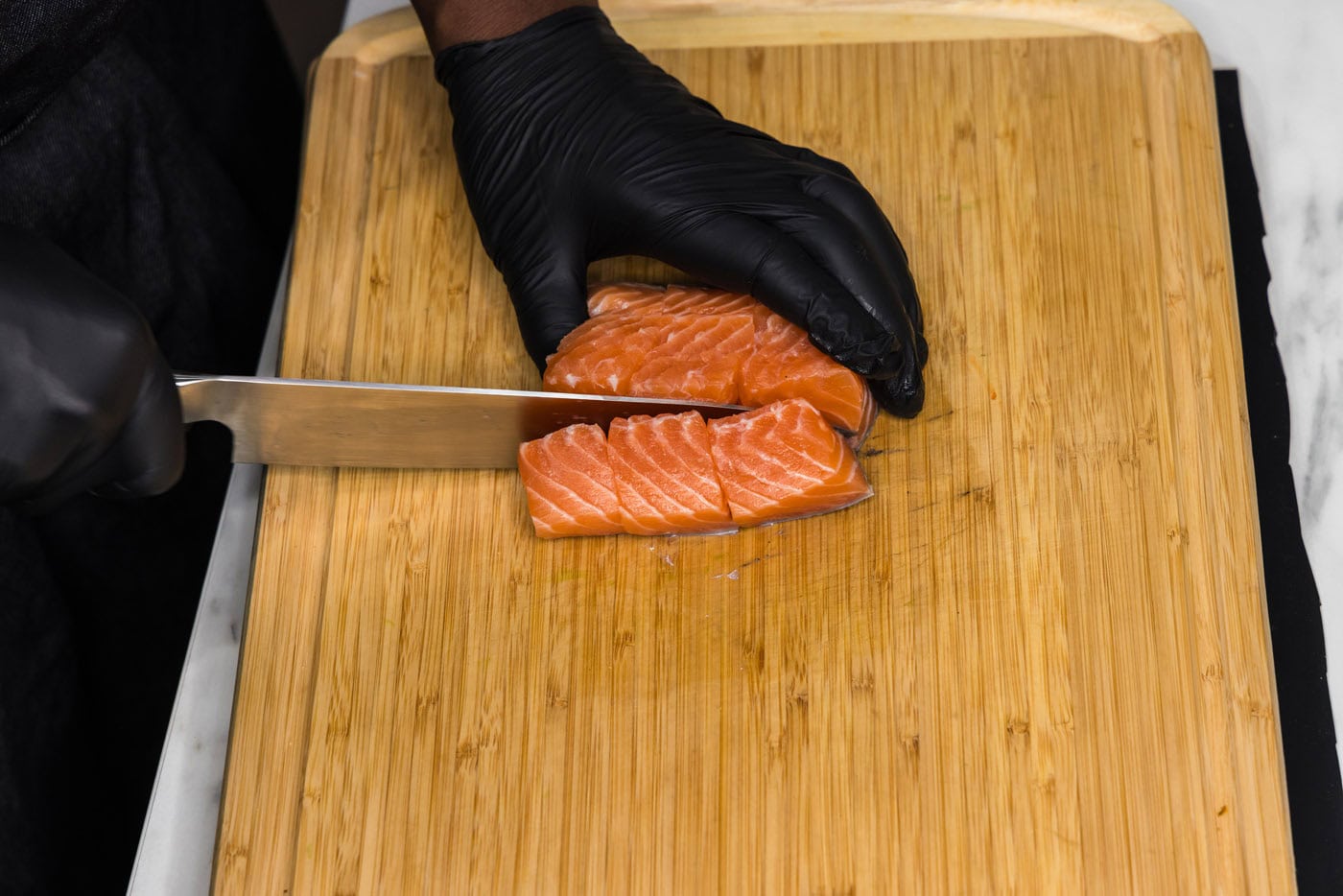 knife slicing salmon into cubes on a cutting board