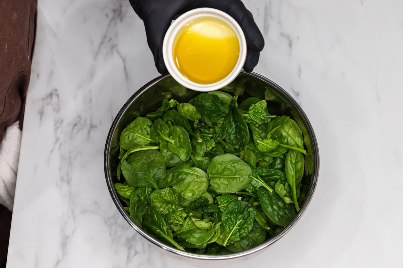 pouring olive oil over fresh spinach leaves