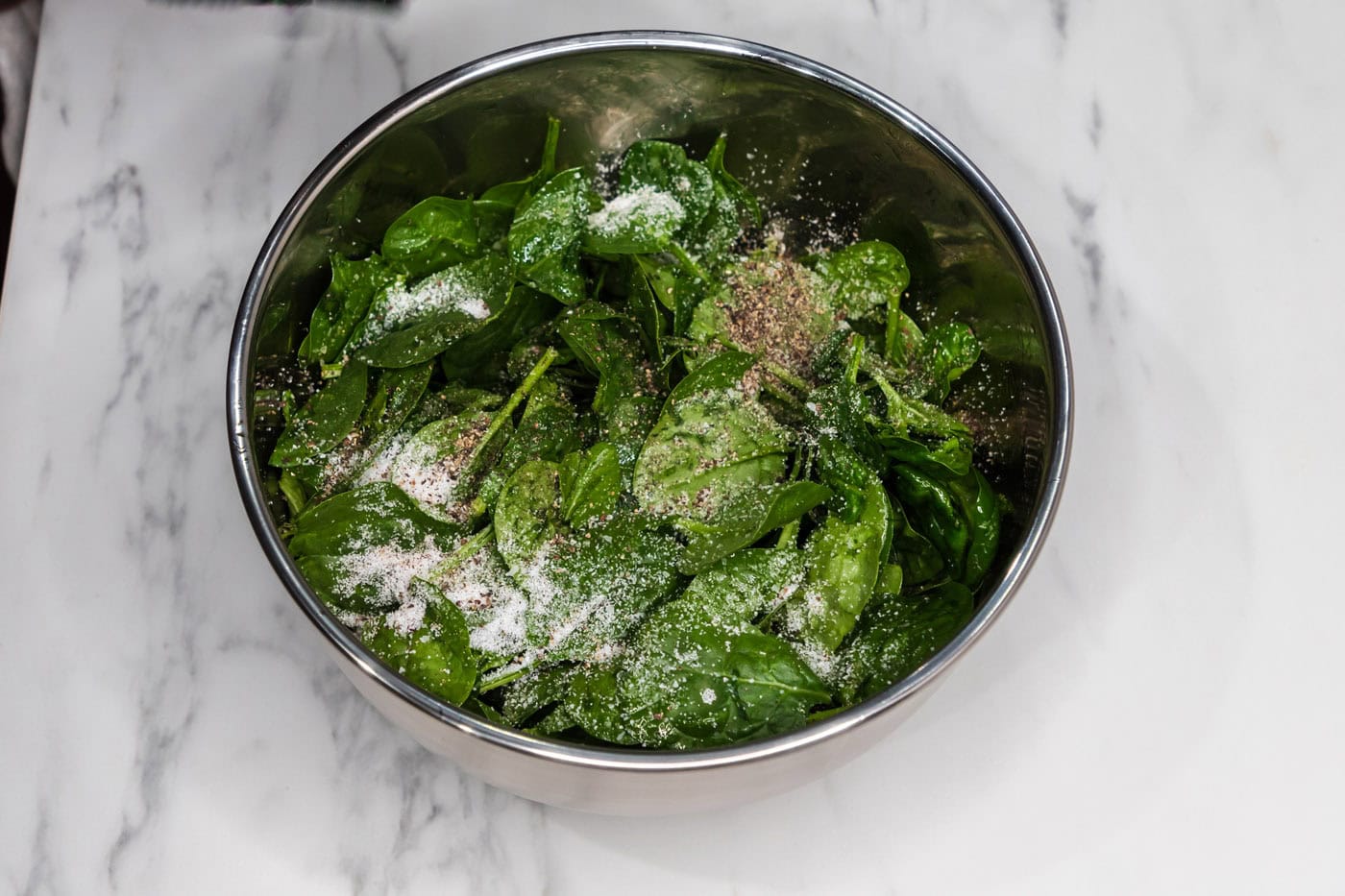 spinach leaves in a bowl with salt, pepper, and olive oil