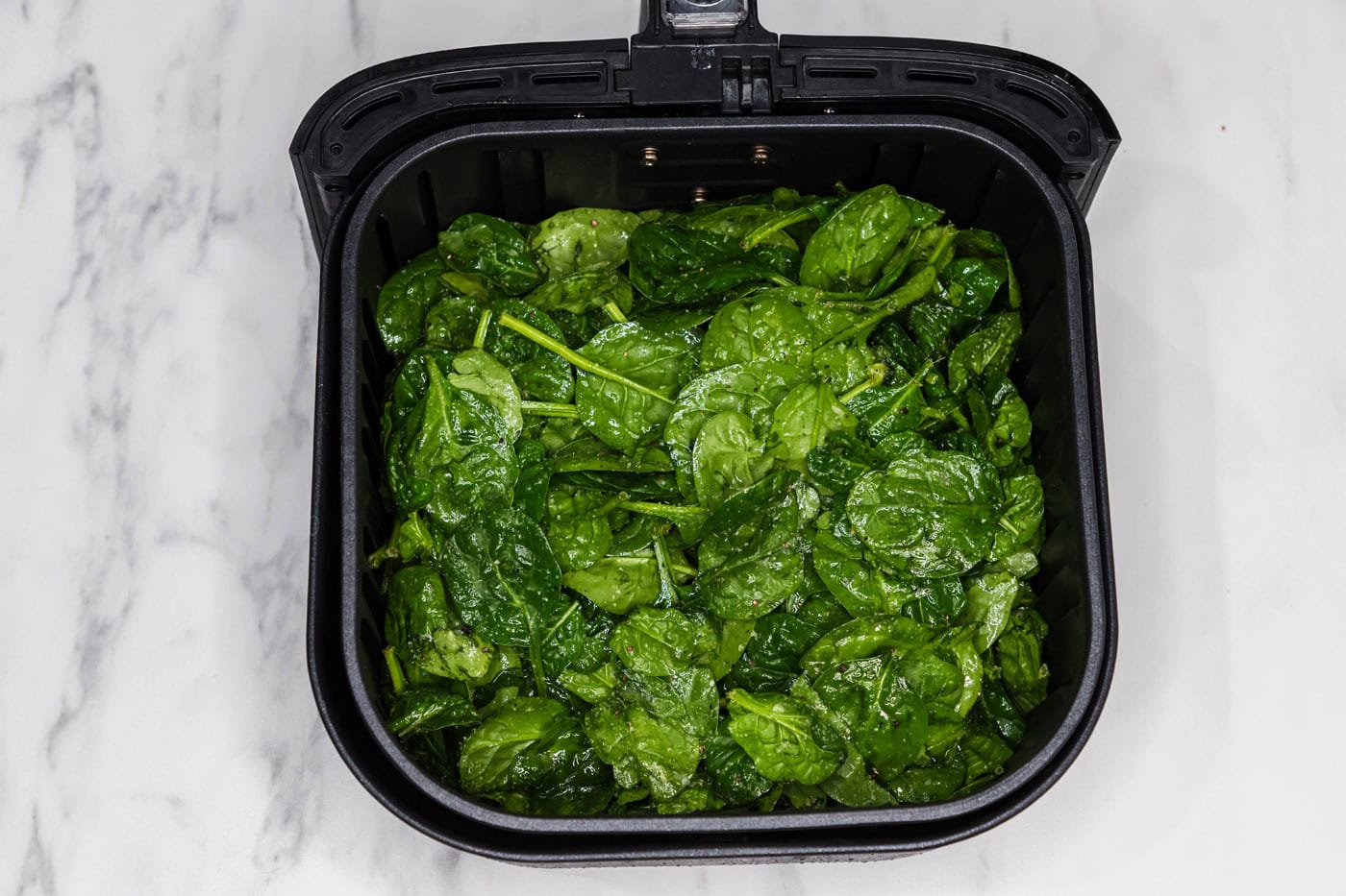 seasoned spinach leaves in an air fryer basket