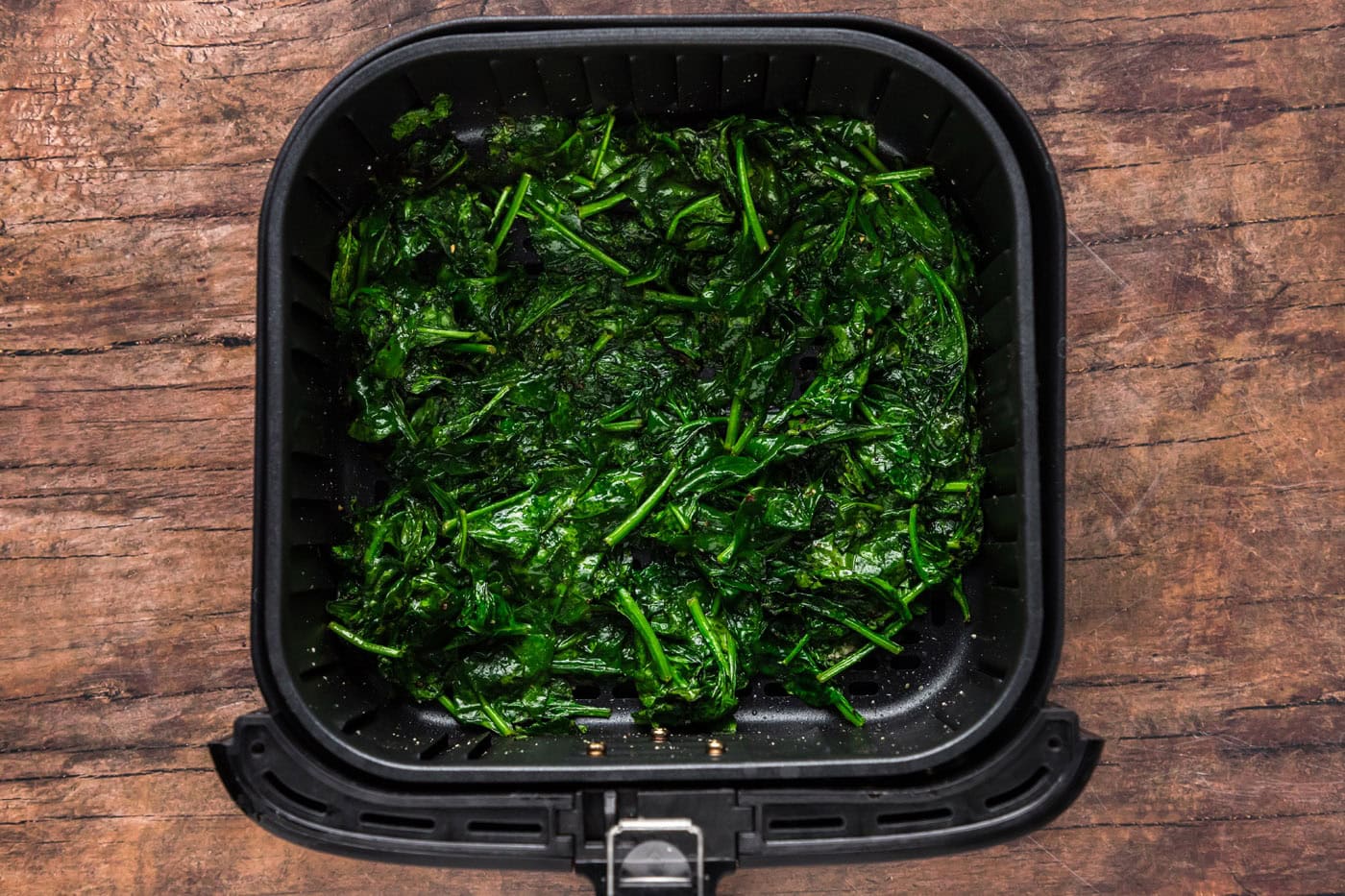 cooked spinach in an air fryer basket