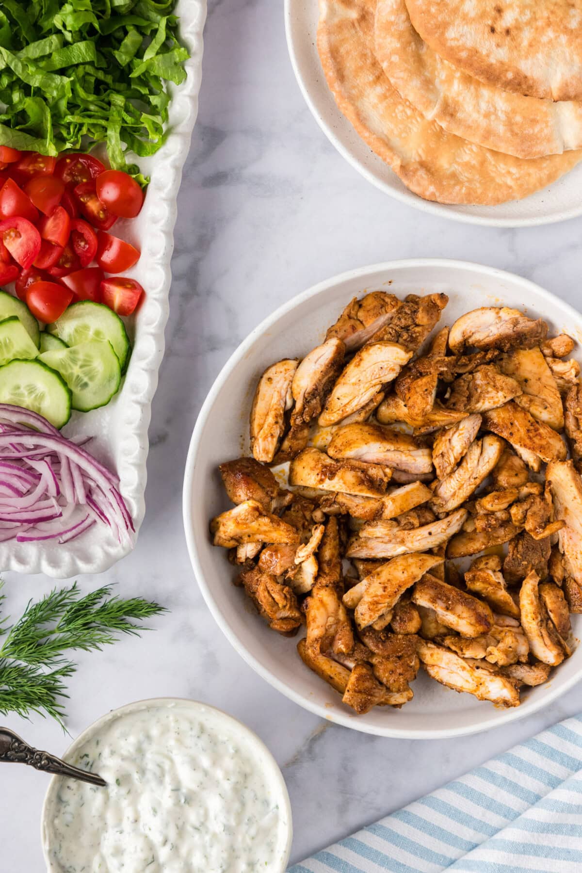 Chicken Shawarma in a bowl with tzatziki, hummus and veggies on the side 