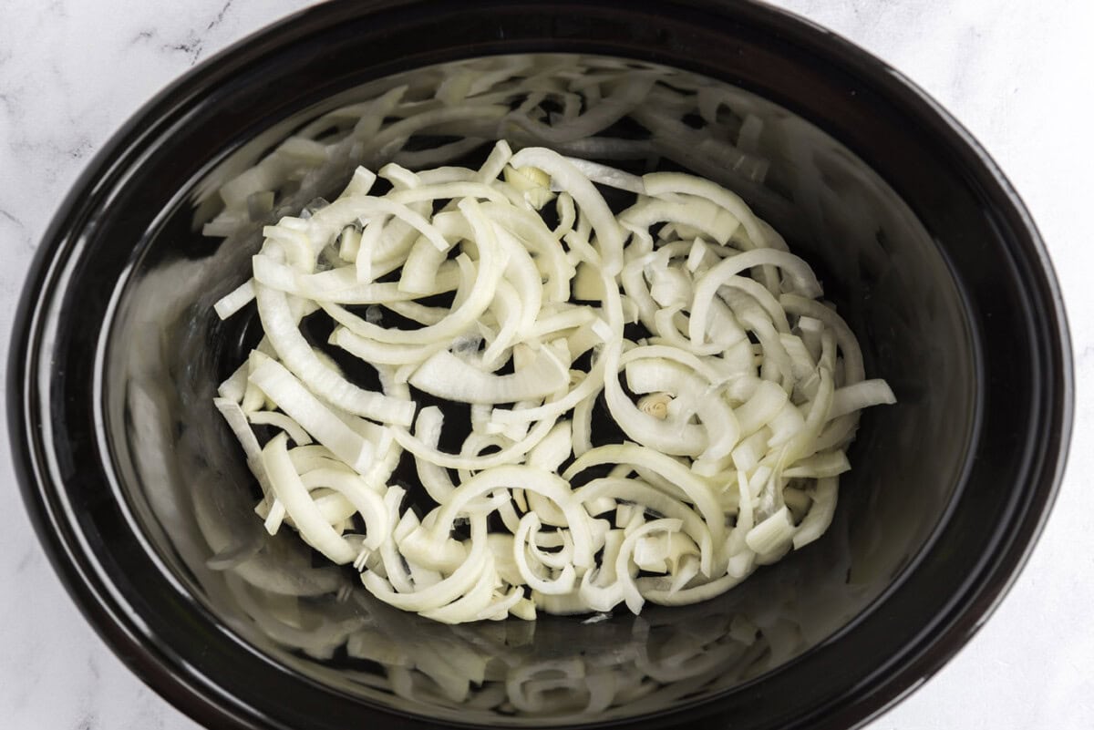 sliced onions on bottom of slow cooker crock
