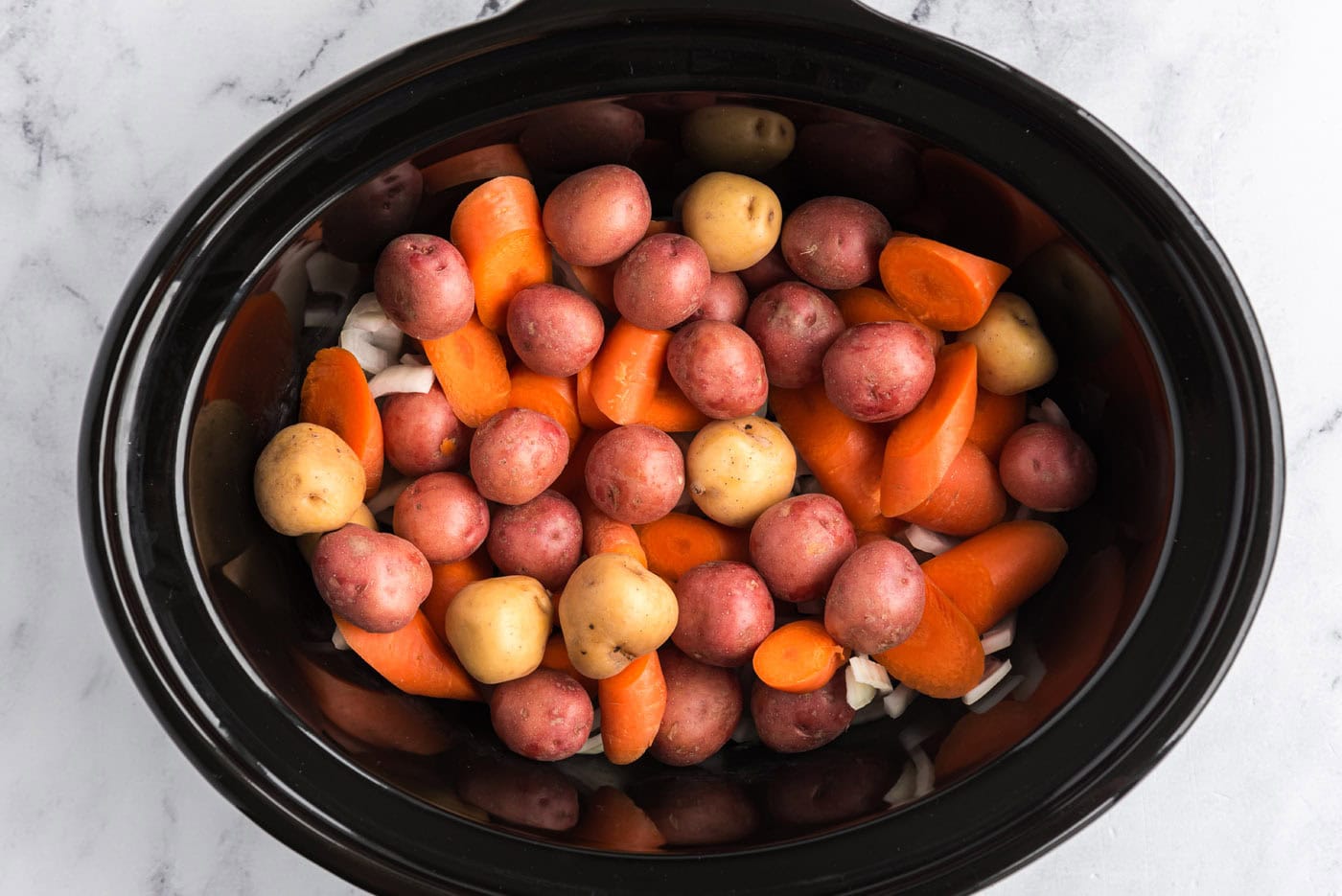 baby potatoes and carrots added on top of onions in slow cooker crock