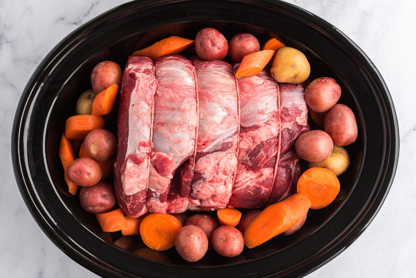 beef roast in crockpot surrounded by carrots and potatoes