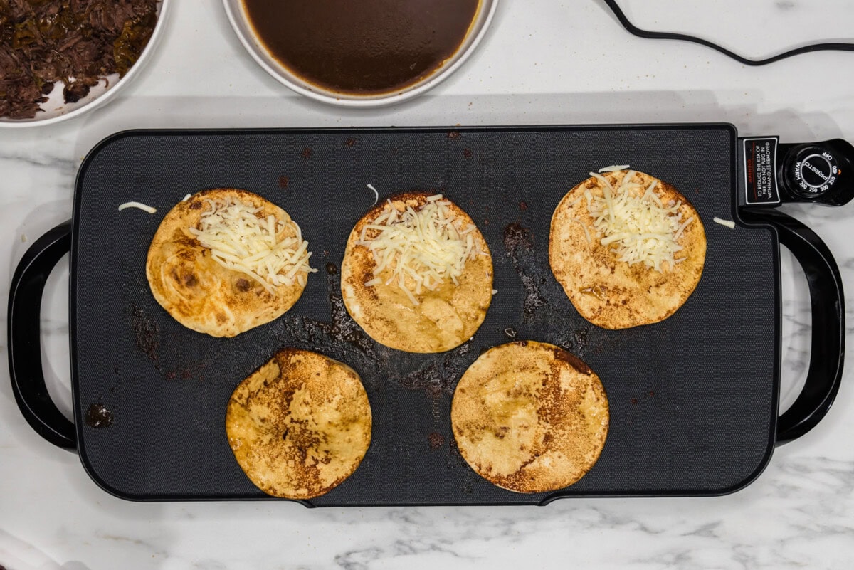 shredded cheese added to tortillas on a griddlee