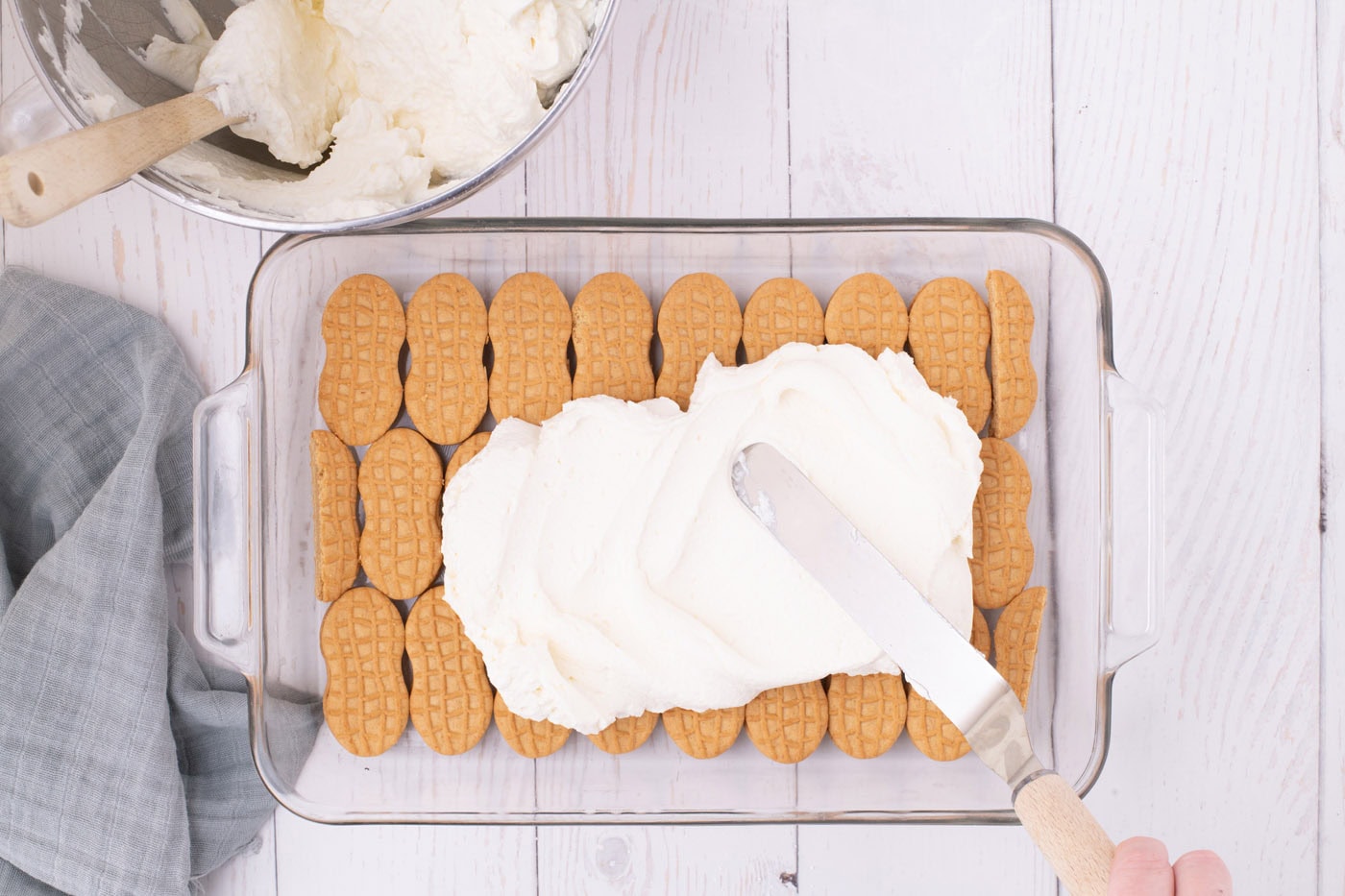 spreading whipped cream cheese layer over nutter butter cookies with an offset spatula