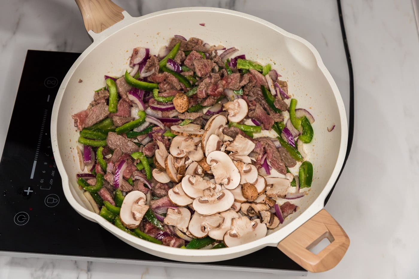 red onion, mushrooms, green bell peppers, and sliced steak in a skillet