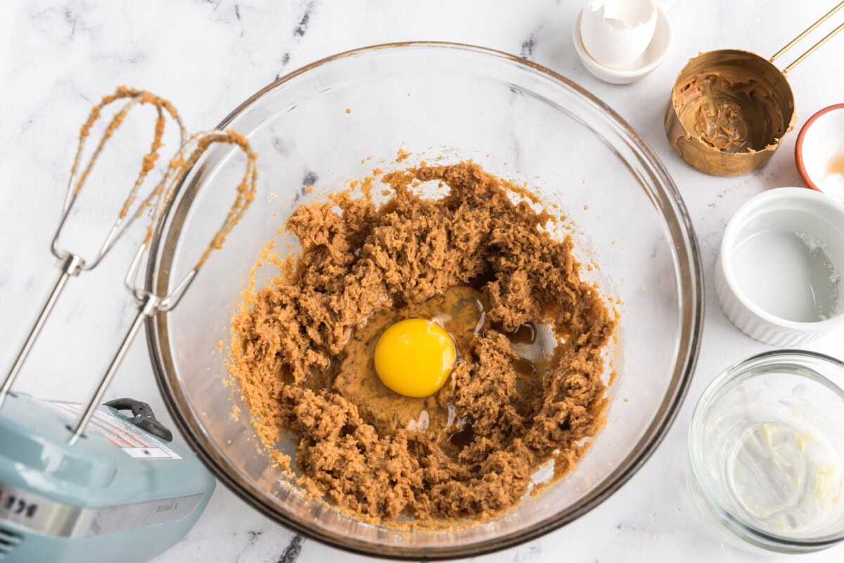adding egg to peanut butter cookie dough in a mixer bowl