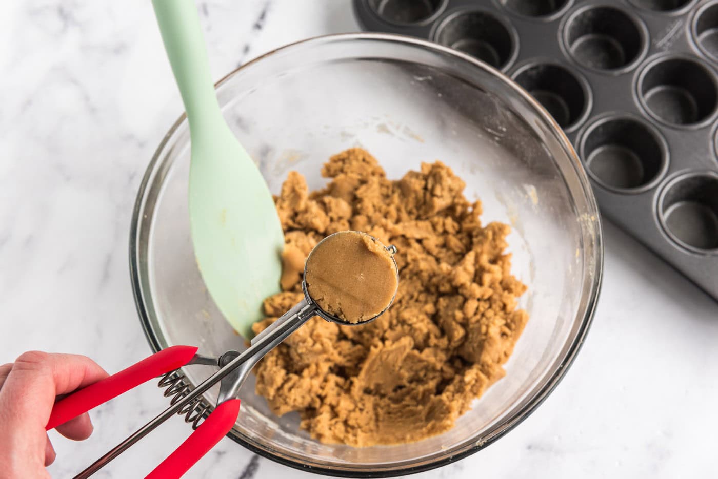 scooping peanut butter cookie dough from bowl with a cookie scoop