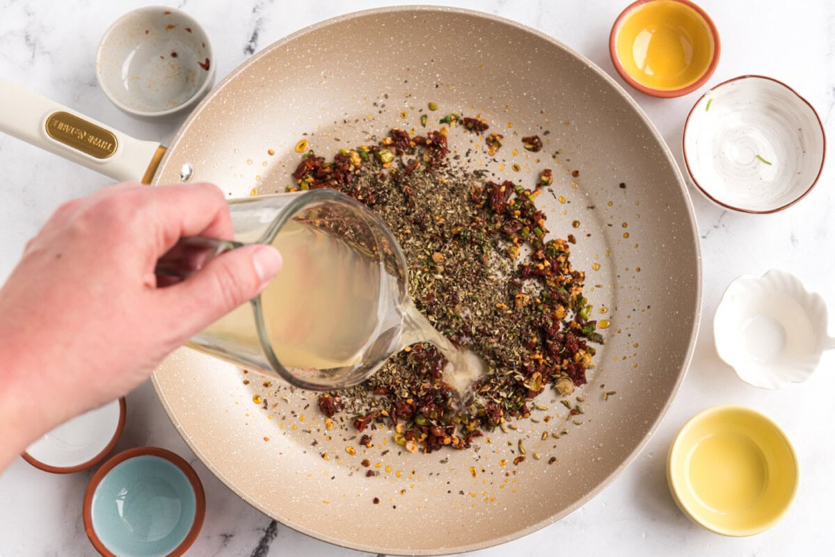 pouring chicken broth into sun dried tomato mixture in a skillet