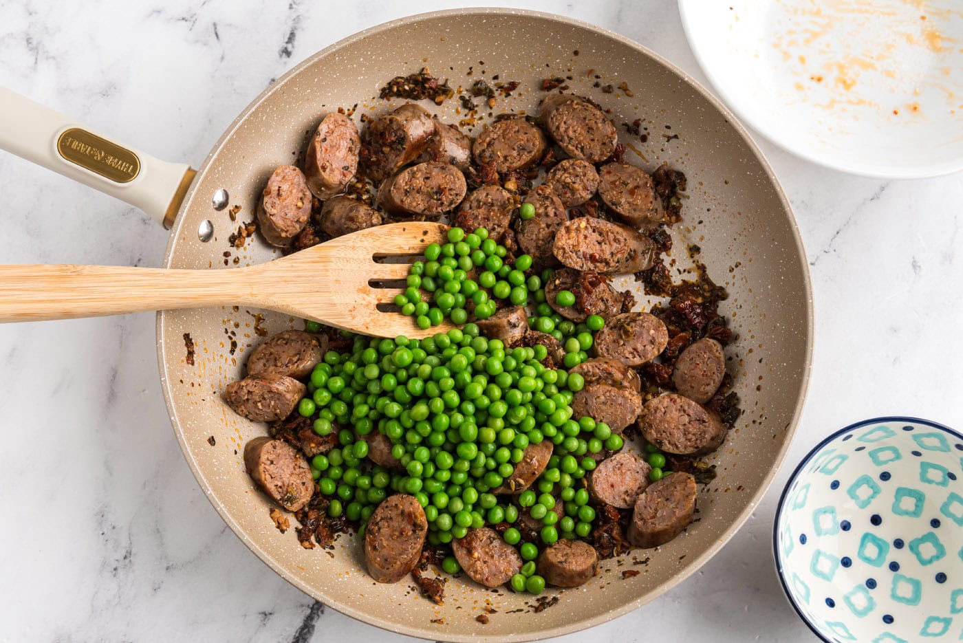 green peas added to Italian sausage and sun dried tomatoes in a skillet