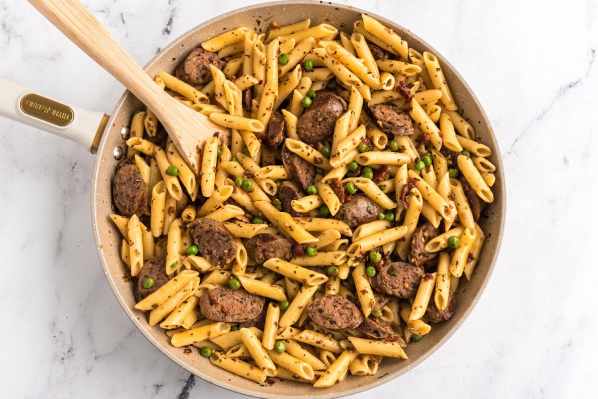 cooked penne pasta added to Italian sausage, peas, and sun dried tomato mixture