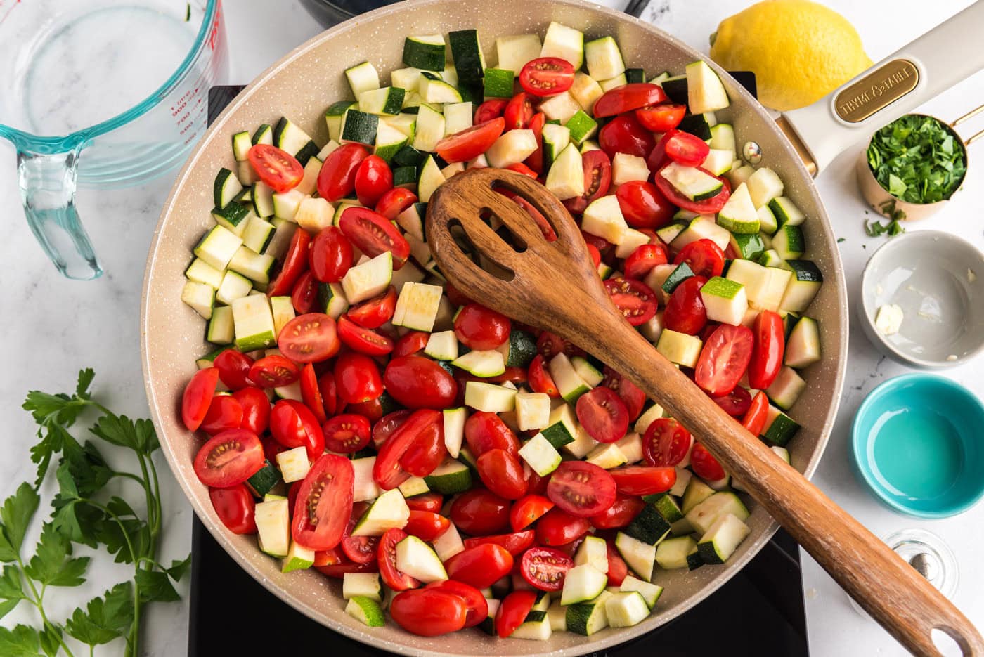 zucchini and grape tomatoes in a skillet with a wooden spoon