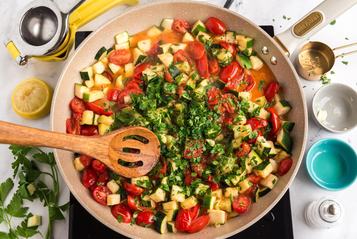 wooden spoon mixing zucchini and tomatoes with parsley in a skillet