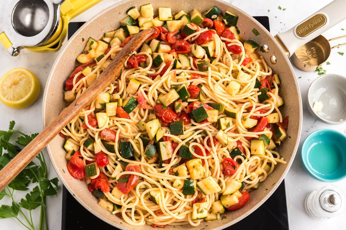zucchini tomato pasta in a skillet with a wooden spoon