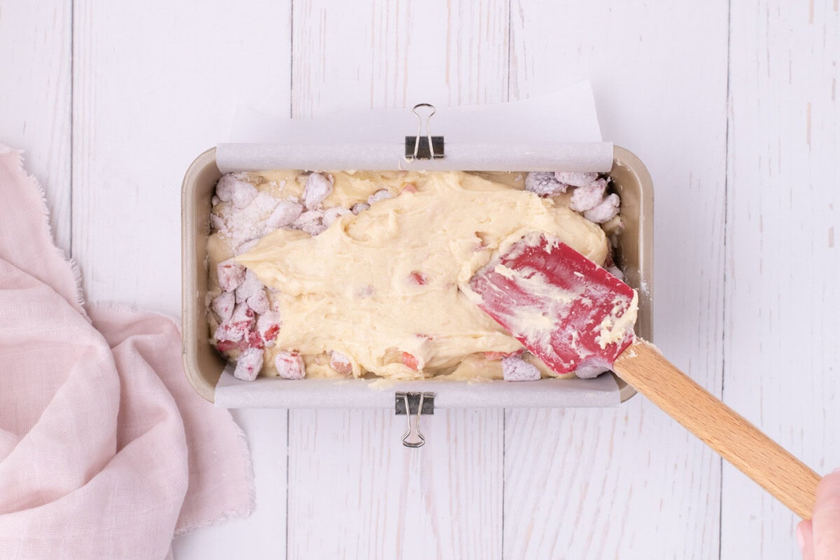spreading strawberry batter over diced strawberries in a loaf pan