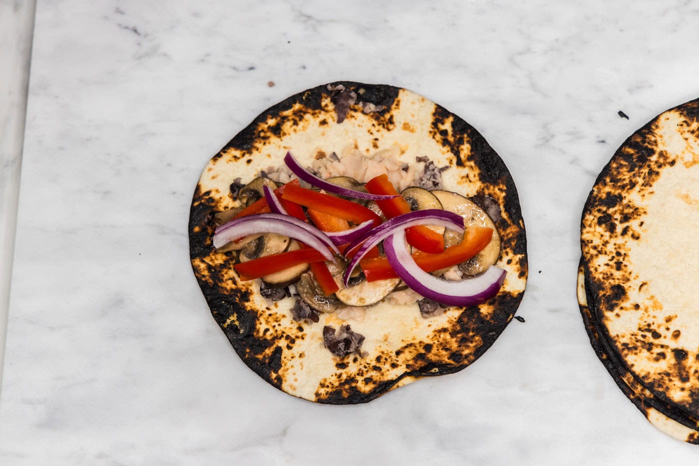 onion, bell peppers, and mushrooms on top of charred tortilla