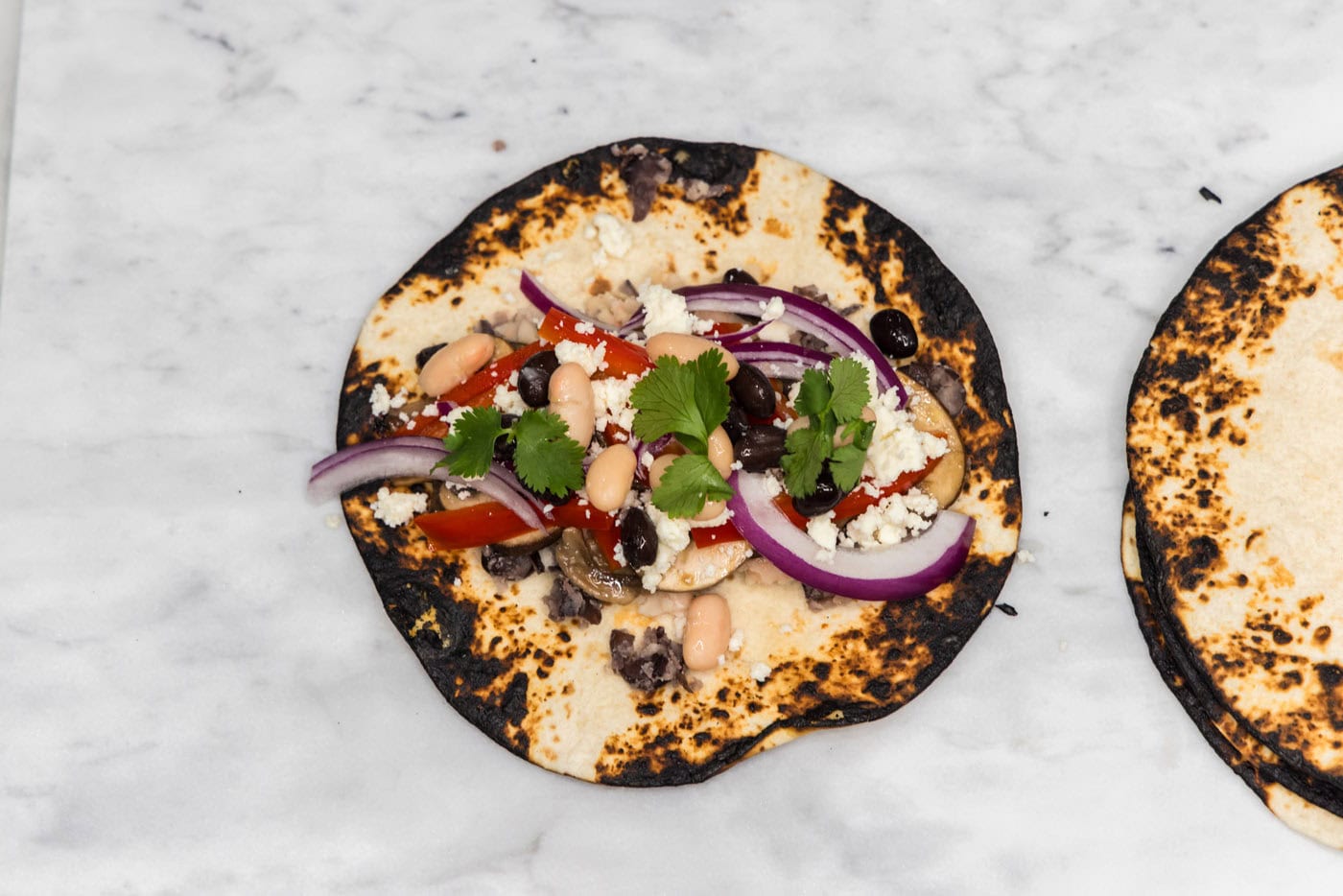 charred tortilla shell topped with fresh vegetables and crumbled queso fresco cheese