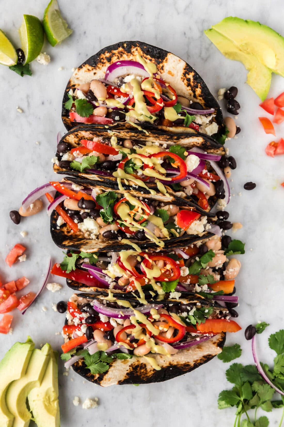 Vegetarian Tacos on a marble platter with tomatoes, limes and avocado slices on the side