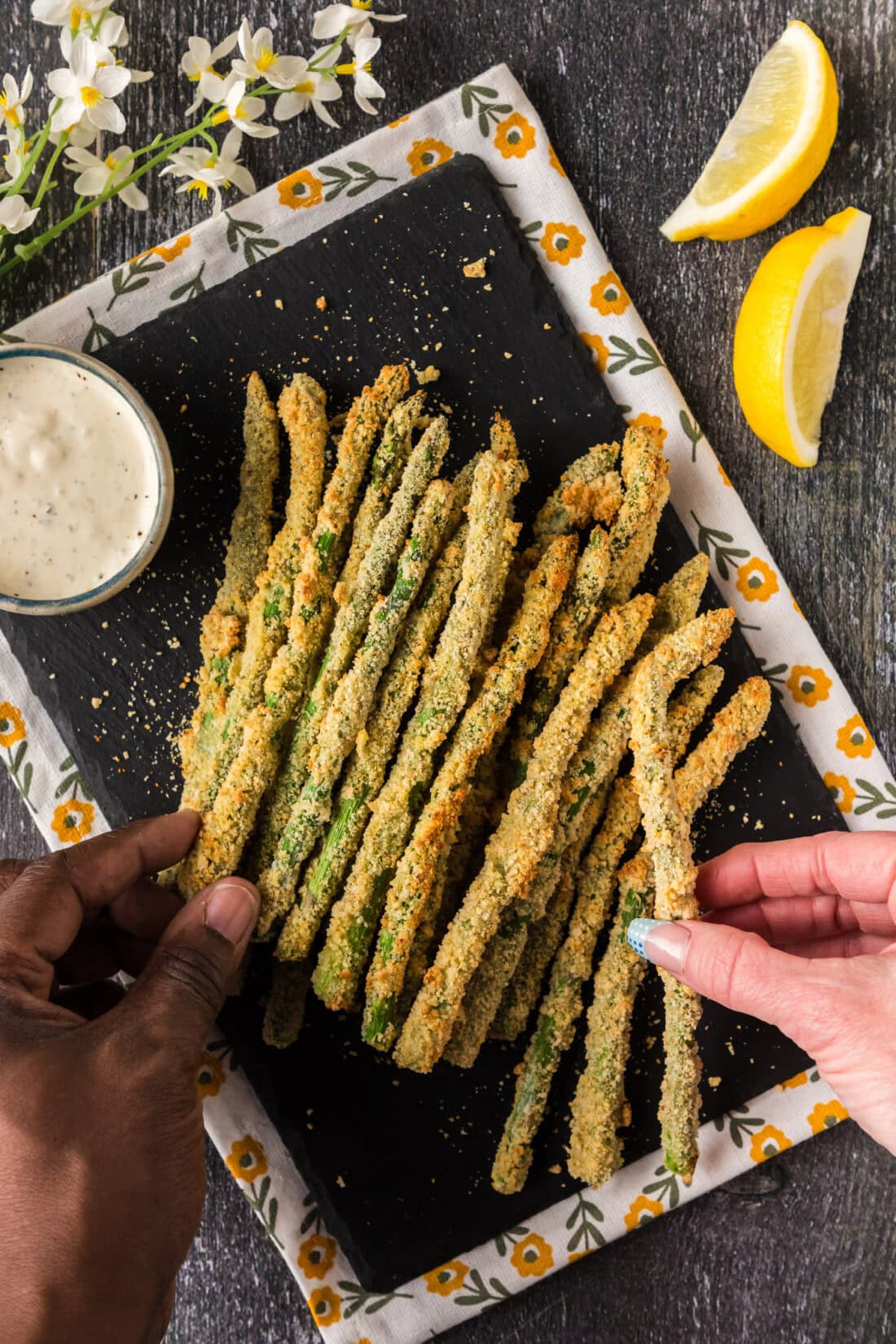 Two hands each picking up an Air Fryer Fried Asparagus spear from a platter