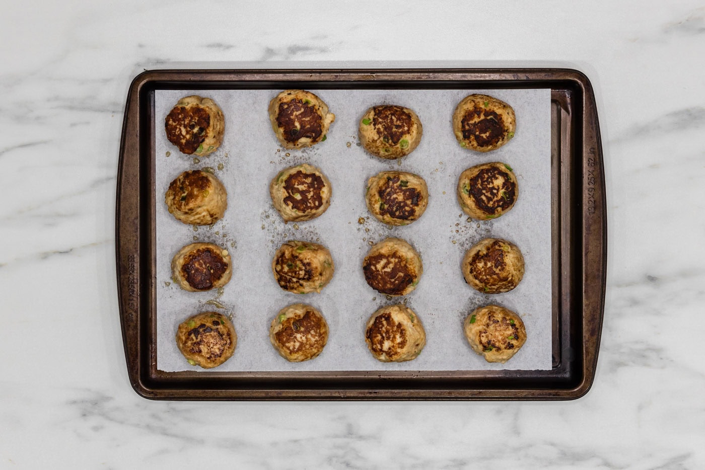 browned chicken meatballs on a parchment lined baking sheet