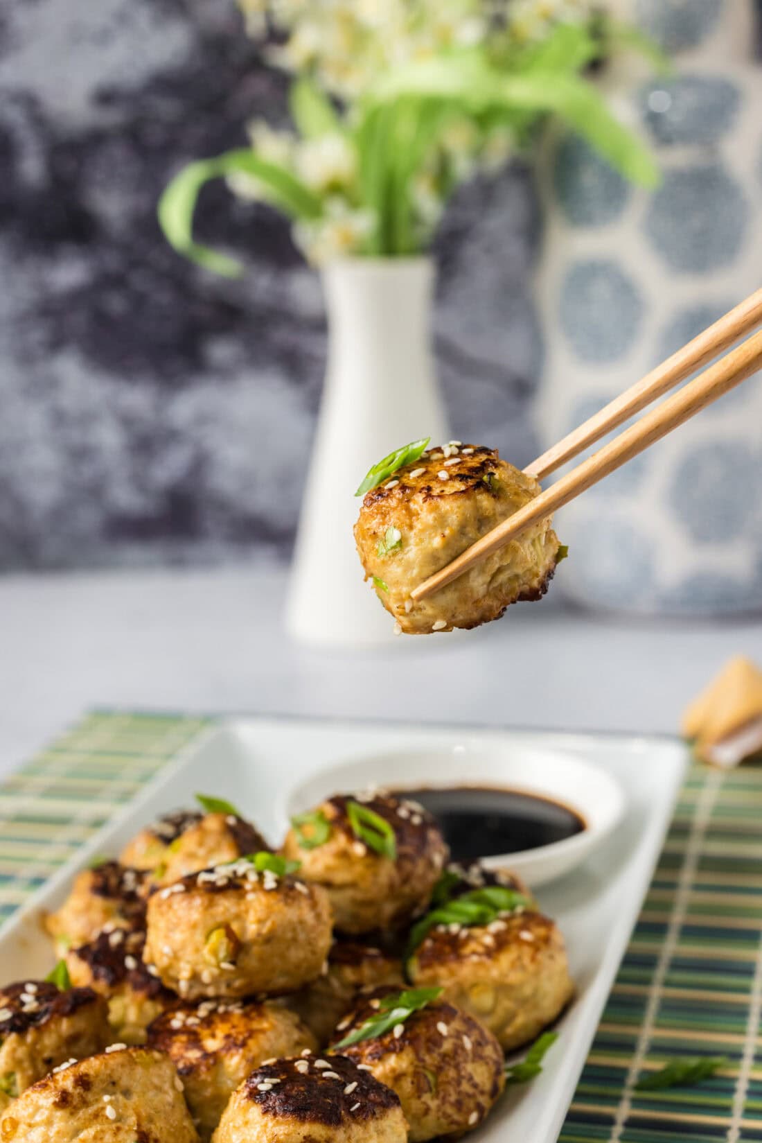 Chopsticks holding an Asian Meatball over a platter of more Asian Meatballs