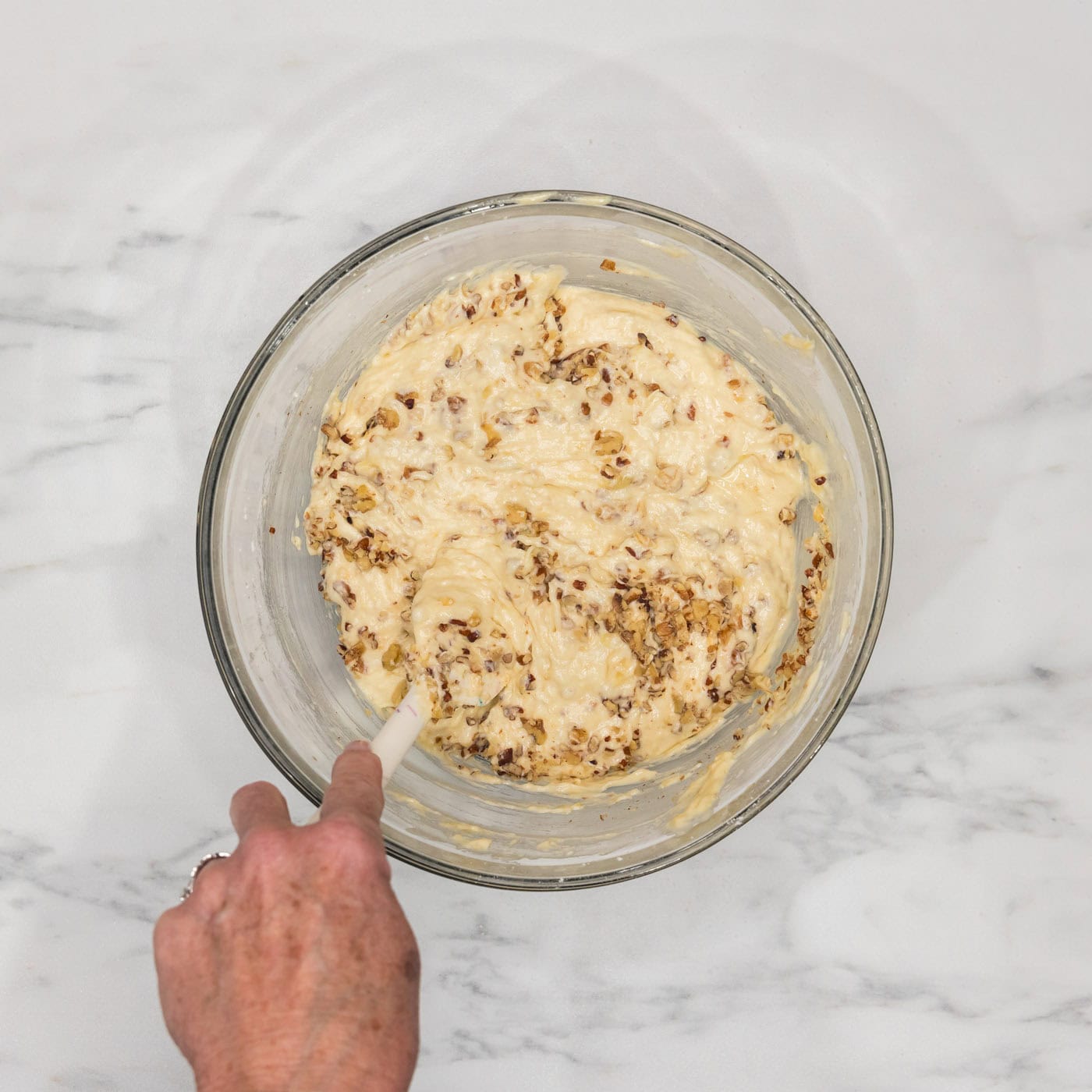 stirring walnuts into bundt cake batter in a bowl
