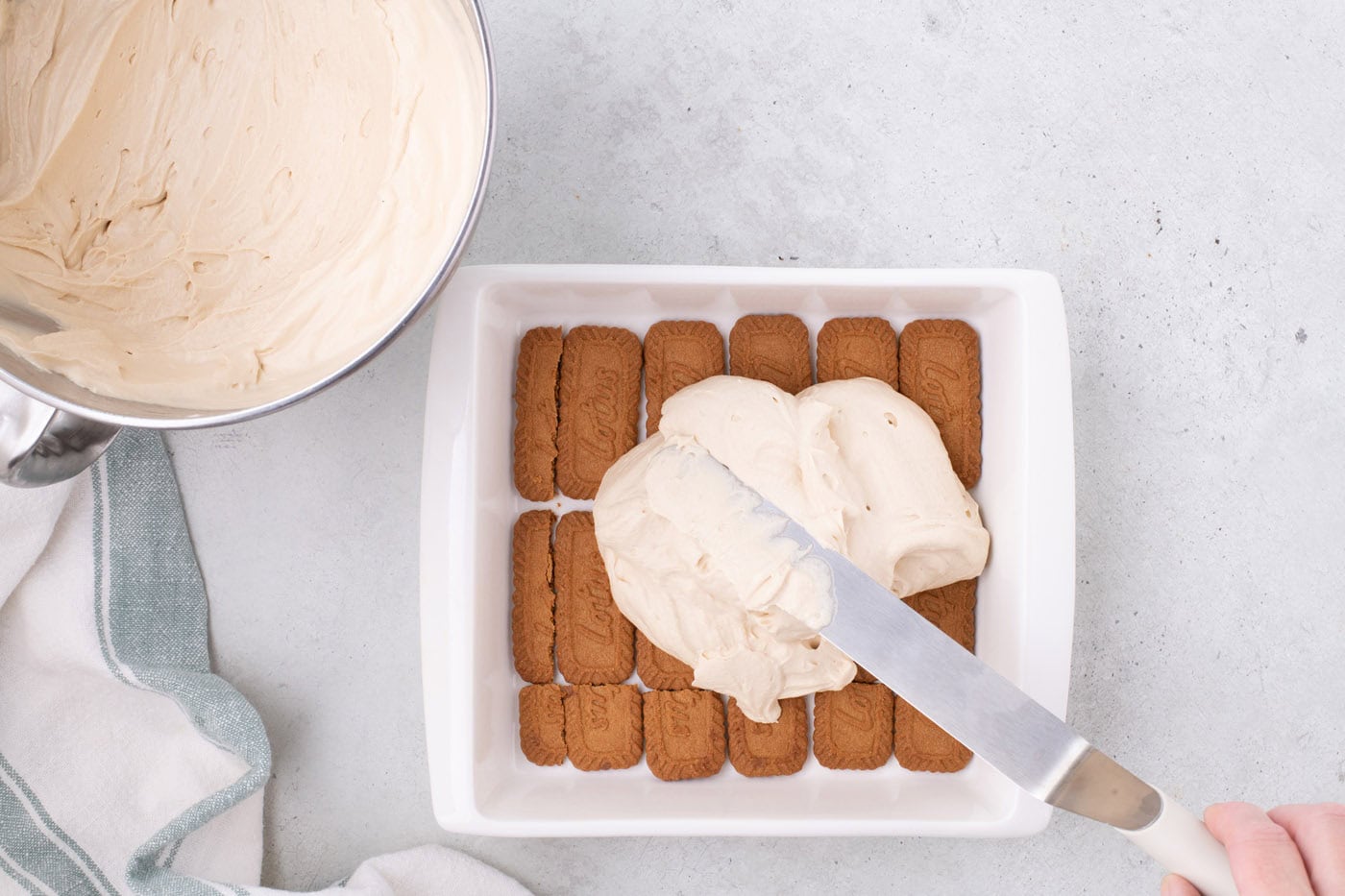 spreading Biscoff cream cheese mixture over cookies in a baking dish