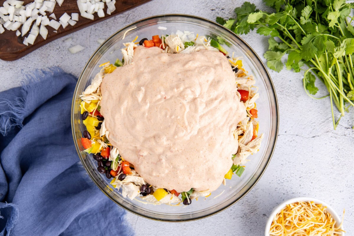 sour cream mixture on top of chicken taco casserole ingredients in a bowl