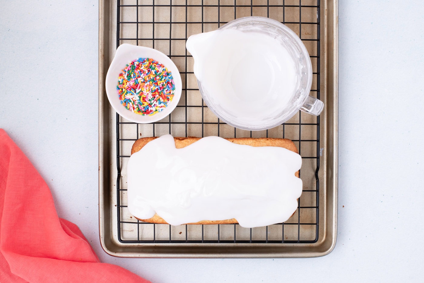 vanilla glaze poured over quick bread with a bowl of sprinkles on the side