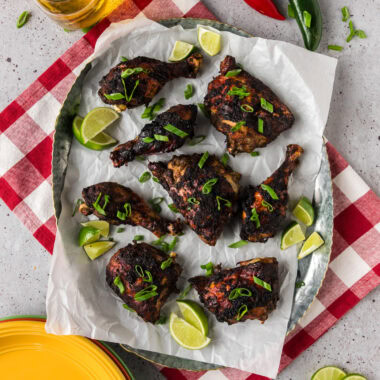 Jerk Chicken on a parchment lined serving tray with limes on the side