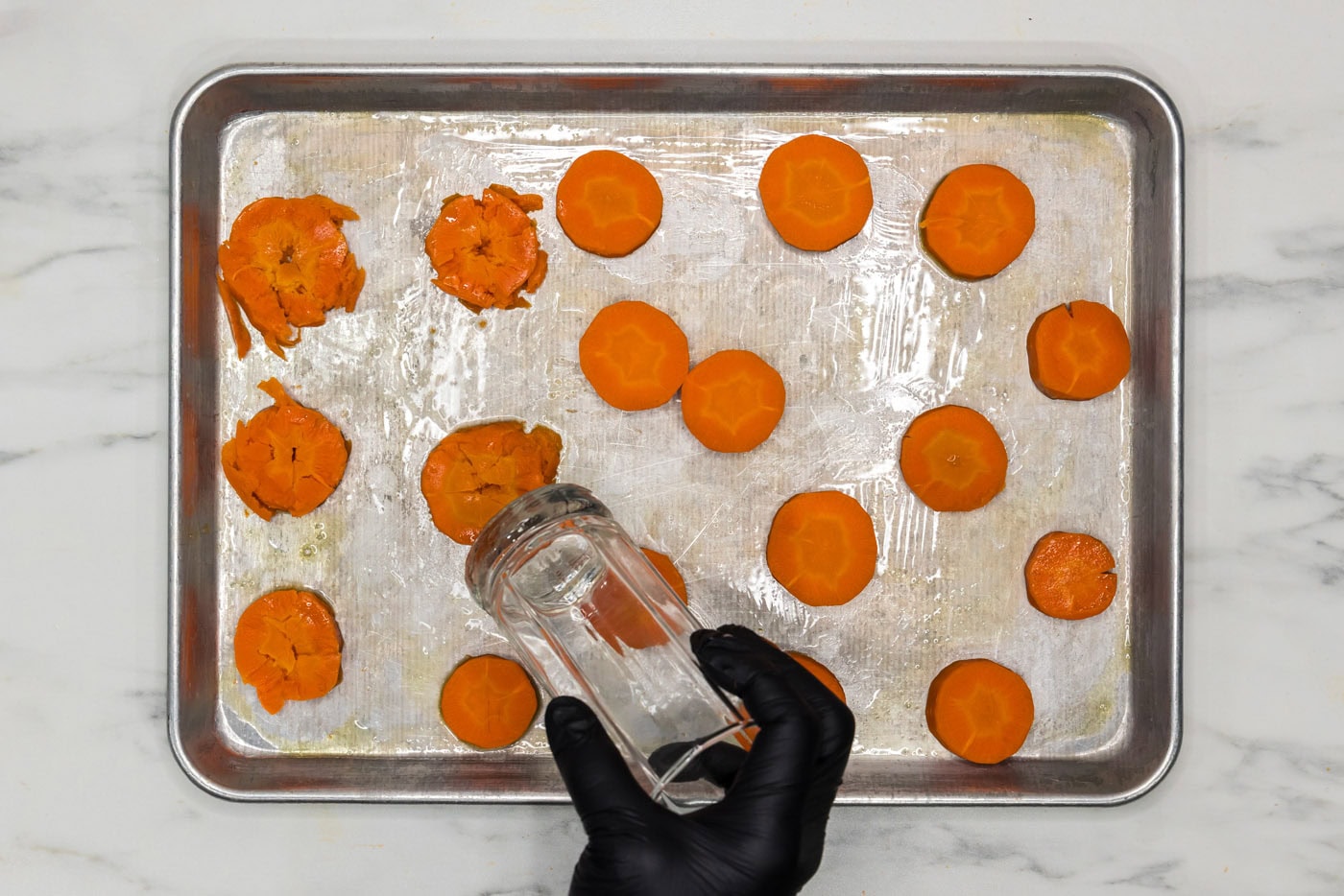 smashed carrots on a baking sheet with the flat end of a drinking glass