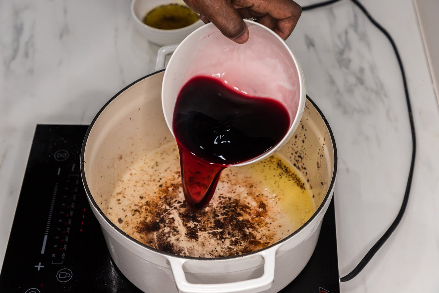 pouring red wine into dutch oven to deglaze