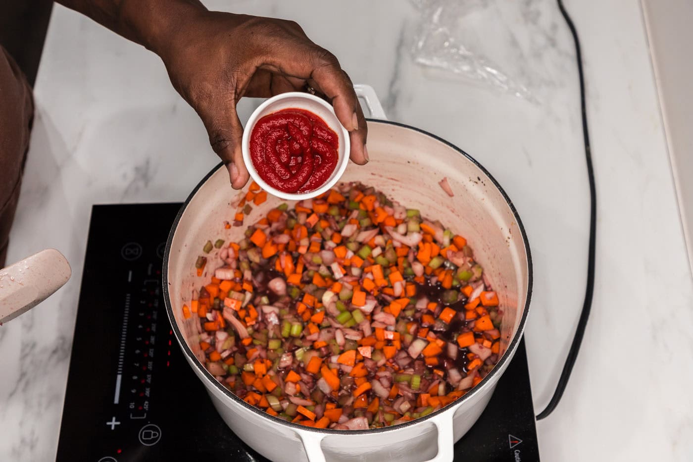 hand holding ketchup over a dutch oven of vegetables and red wine