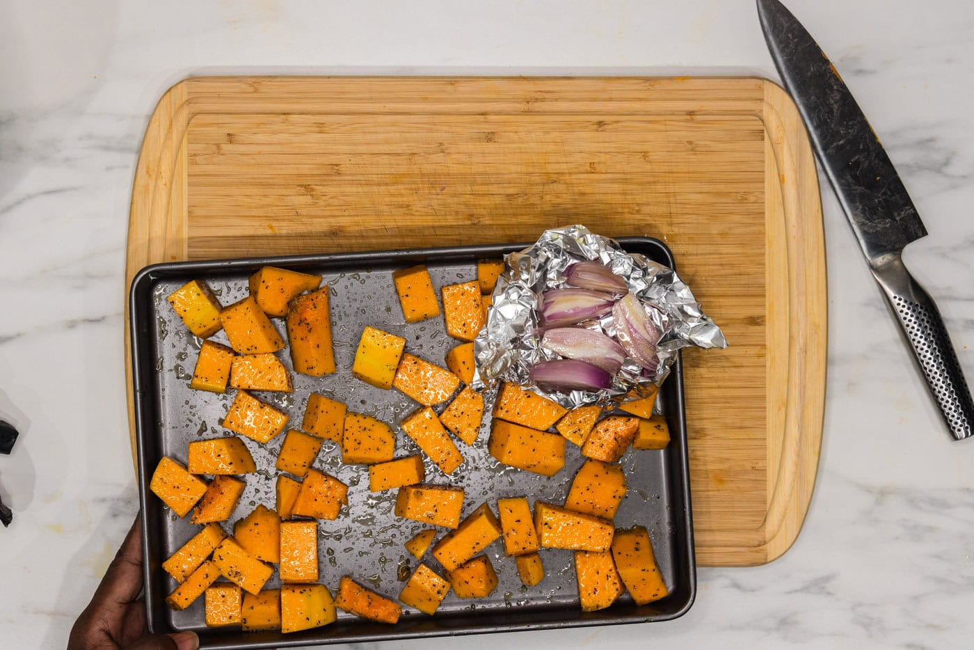 butternut squash cubes on a baking sheet with shallots in a foil packet