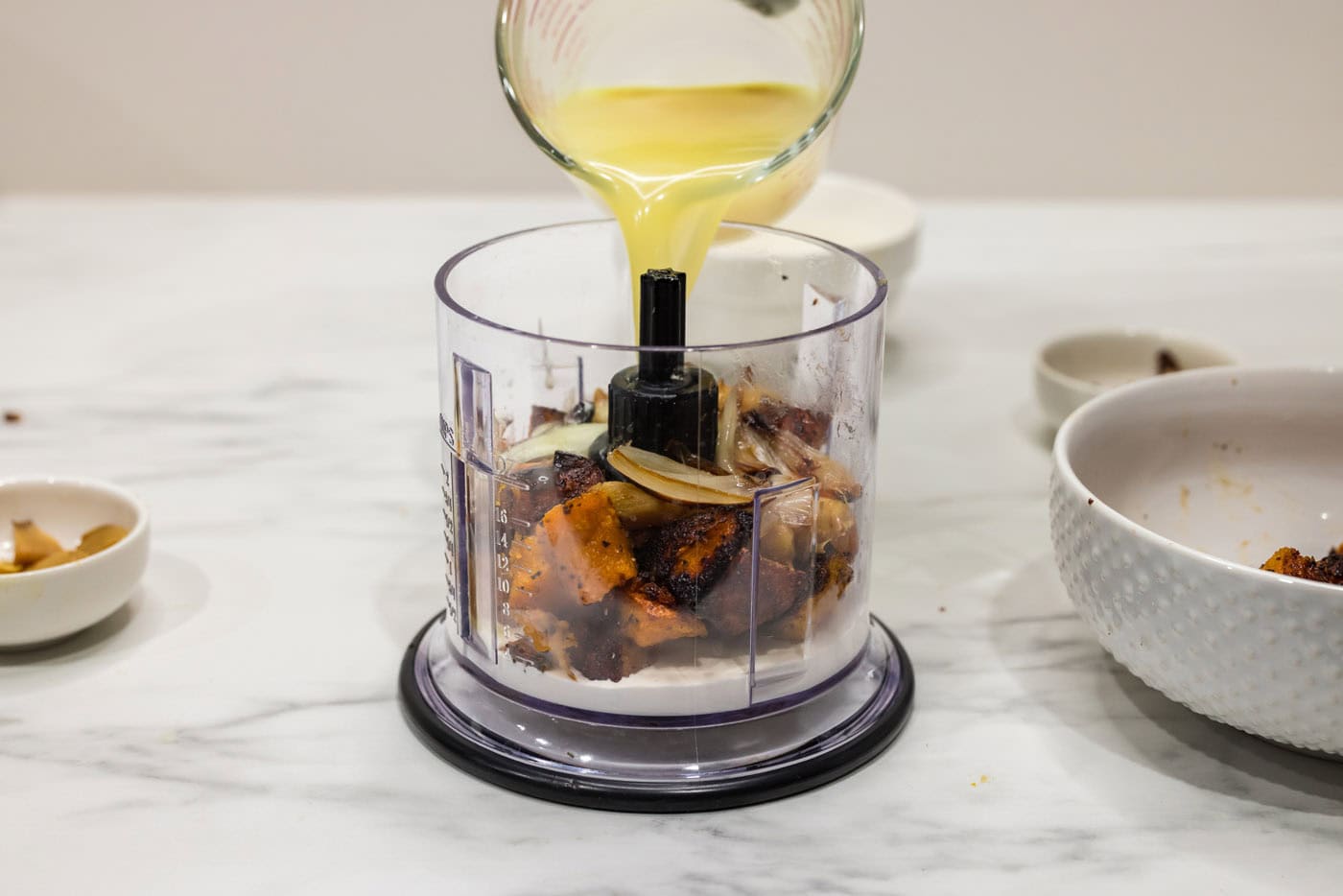 pouring chicken broth into mini food chopper with squash and shallots