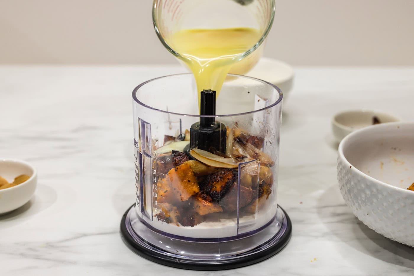 pouring broth into food chopper with butternut squash, garlic, and shallots