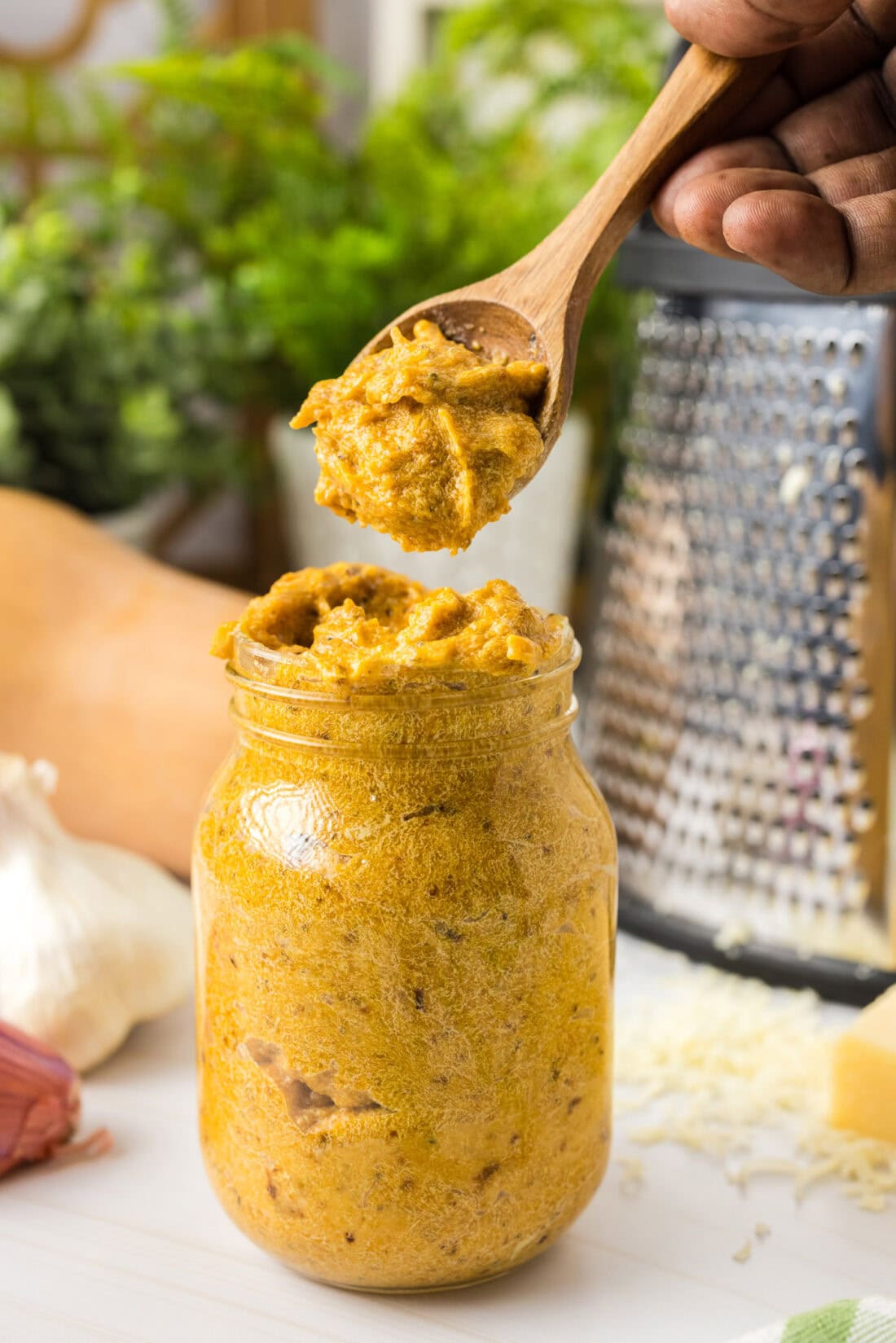 Spoonful of Butternut Squash Pasta Sauce held above a jar of Butternut Squash Pasta Sauce