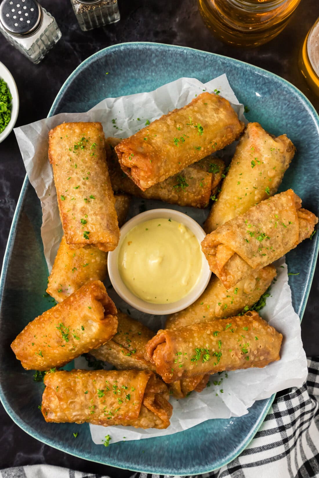 Corned Beef Egg Rolls on a blue platter with a bowl of dipping sauce in the middle