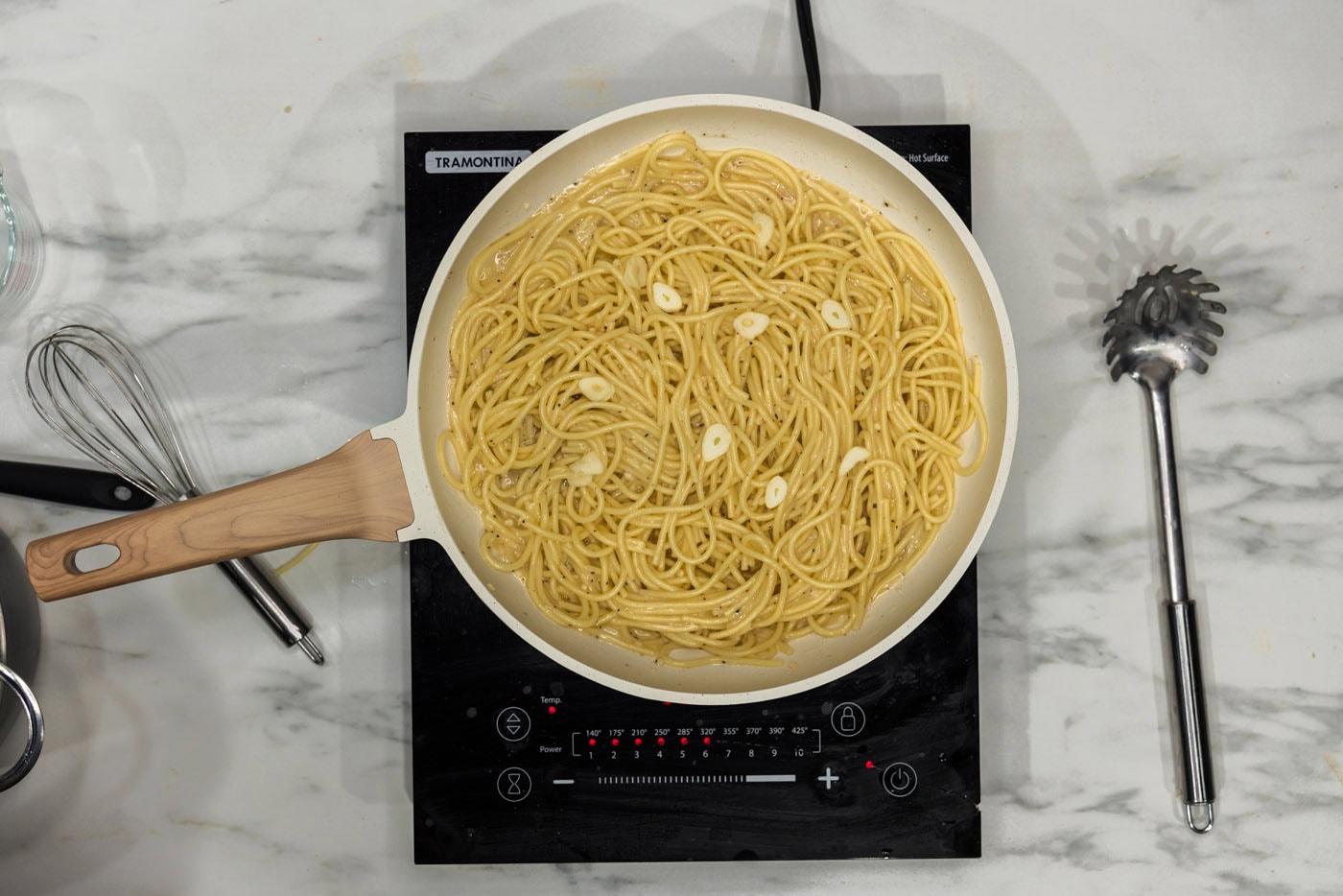 slivered garlic added to pasta with garlic butter sauce in a skillet