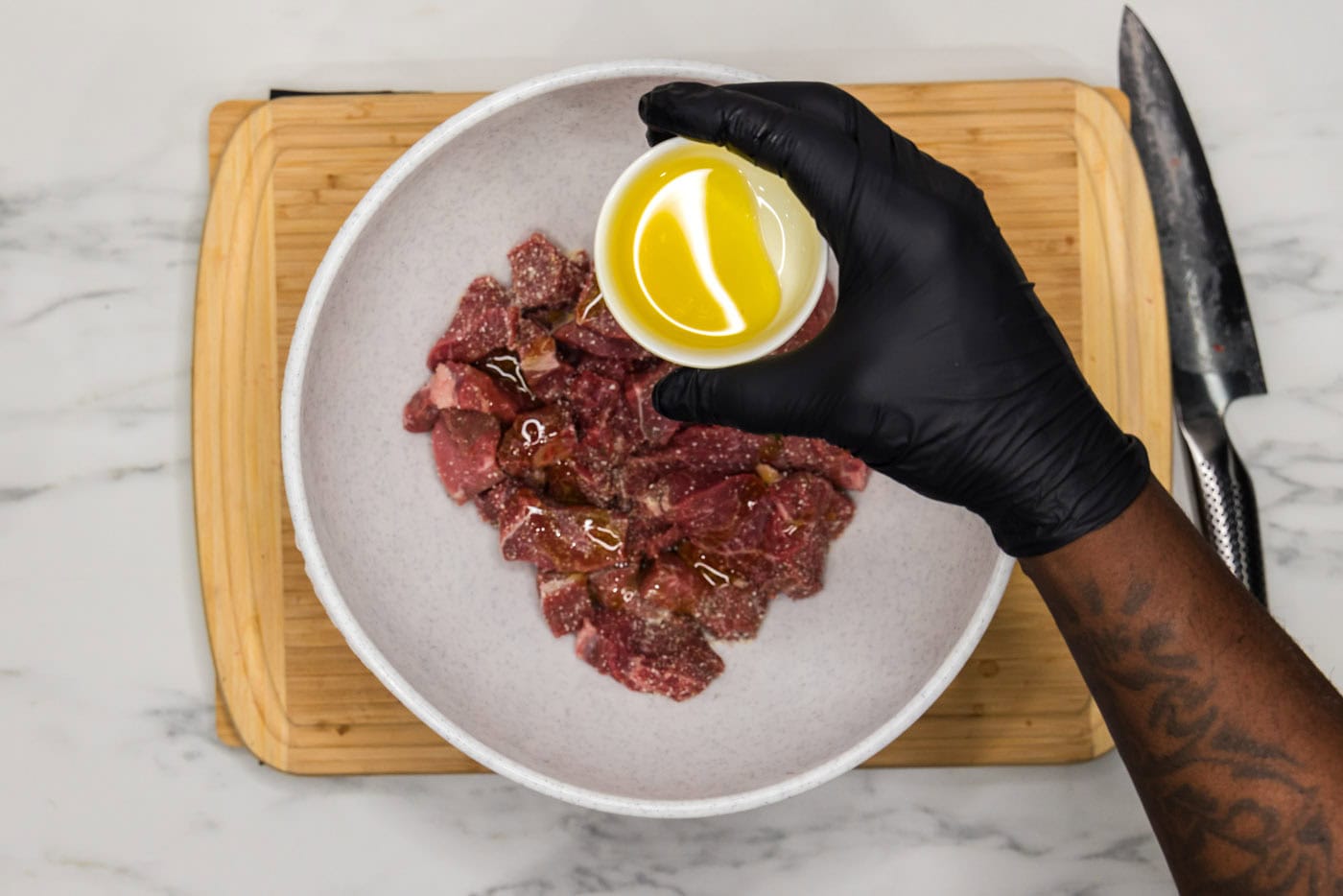 hand holding bowl of olive oil over cubes of meat