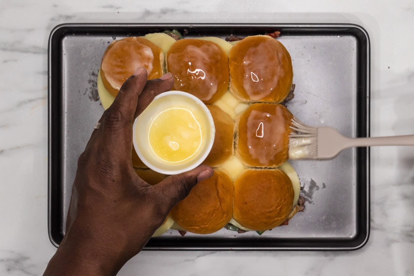 basting philly cheesesteak sliders with melted butter