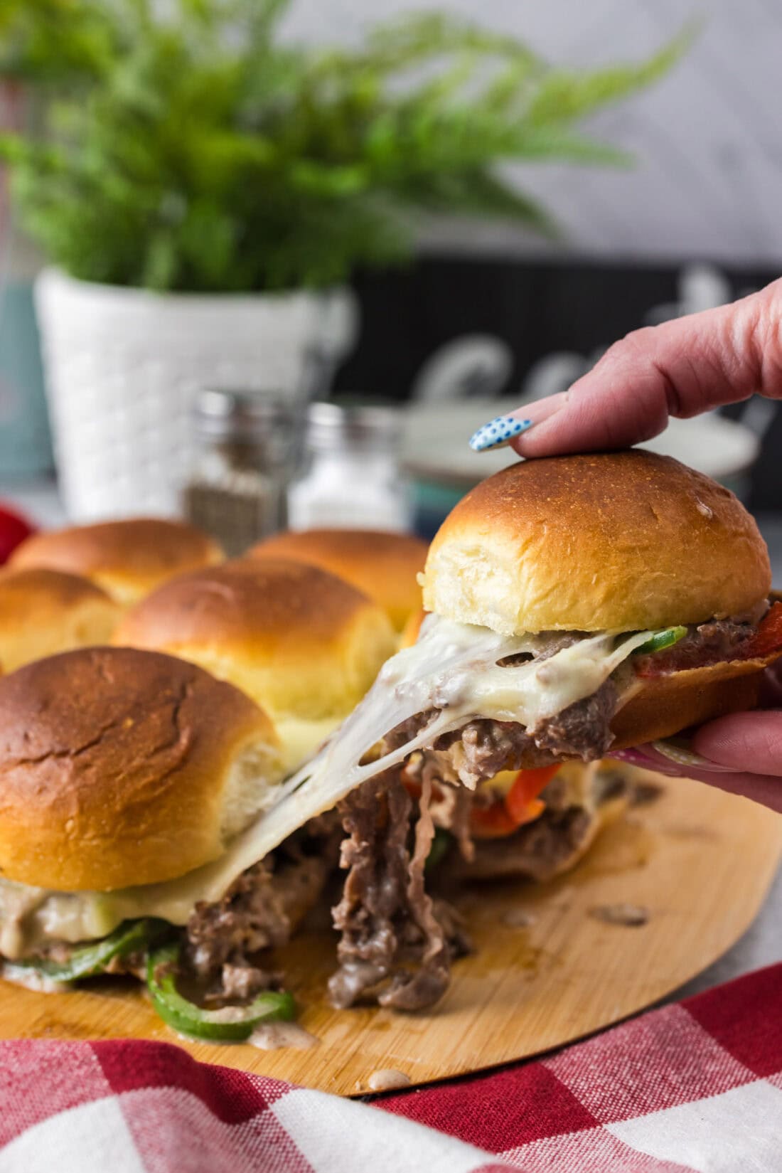 Hand pulling up a cheesy Philly Cheesesteak Slider from the board of Philly Cheesesteak Sliders