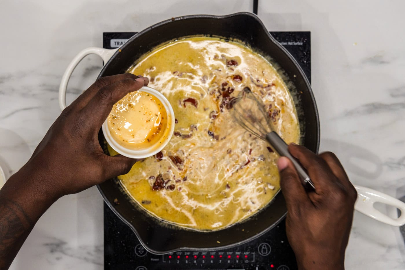 whisking chicken base into skillet with red onion, garlic, and heavy cream