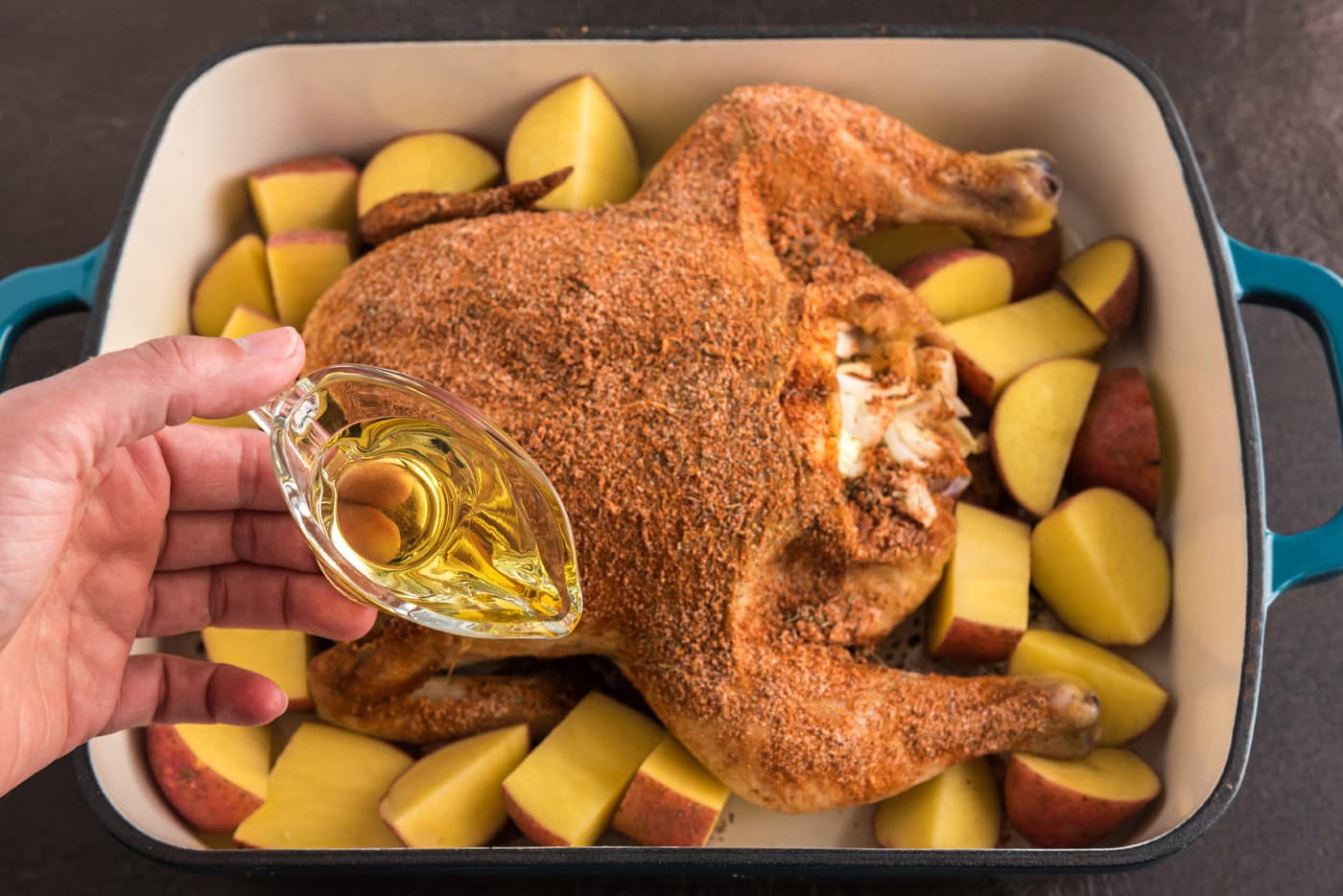 pouring olive oil into pan with whole chicken and red potatoes