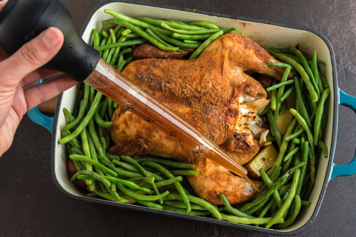 basting chicken and green beans in a roasting pan