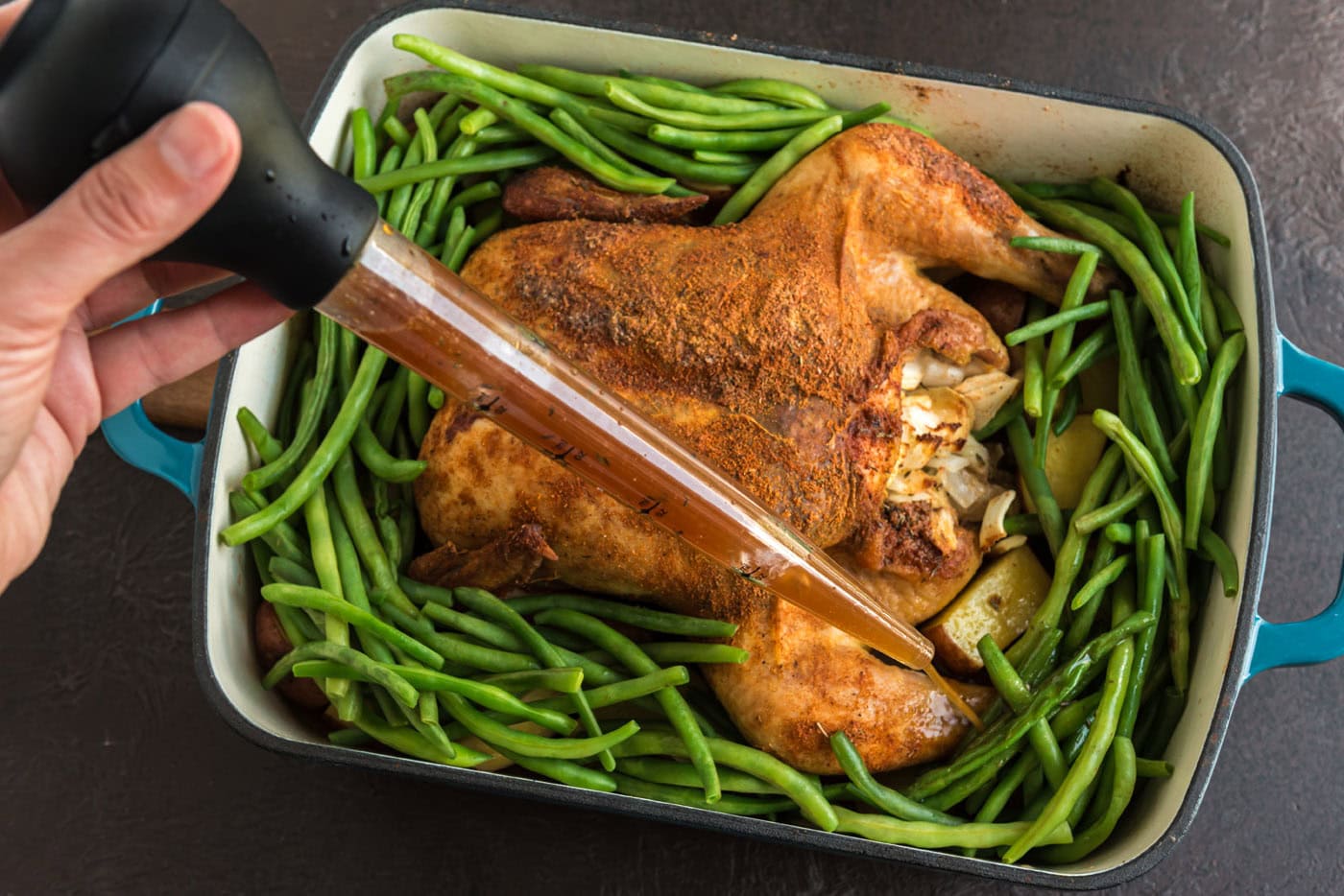 basting chicken and green beans in a roasting pan