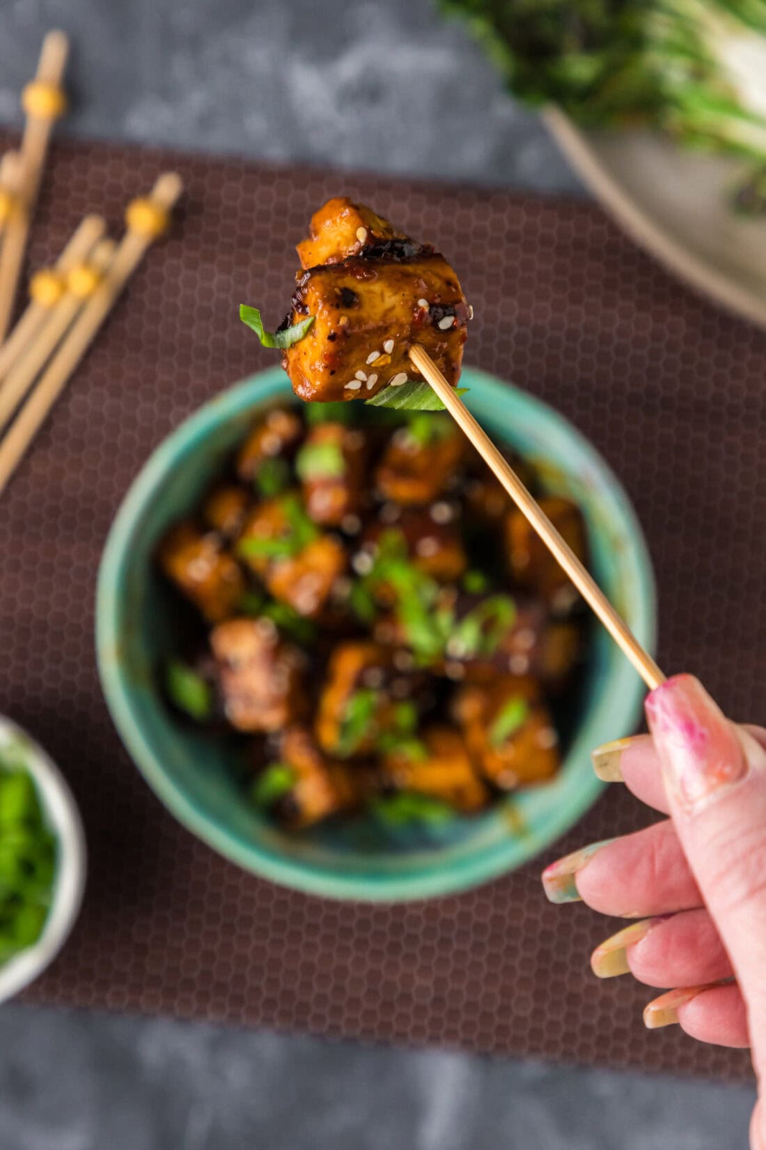 Spicy Tofu on a toothpick held above a bowl of Spicy Tofu